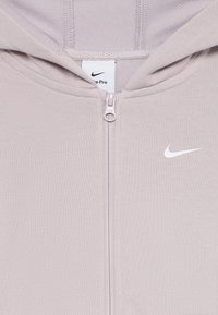 Lys lilla Nike Pro hettegenser med full glidelås, hette og hvit Nike swoosh-logo på høyre brystområde.