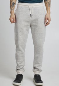 Pantalones de chándal gris claro con un patrón texturizado, que cuentan con una cintura elástica con cordones y puños acanalados. Combinados con zapatos negros.