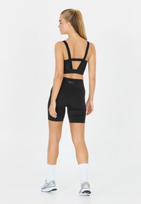 Mustat urheilurintaliivit, joissa on leveät hihnat ja verkkokohdistukset, yhdistettynä mustiin pyöräilyshortseihin, joissa on hengittävää kangasta ja heijastavia yksityiskohtia.