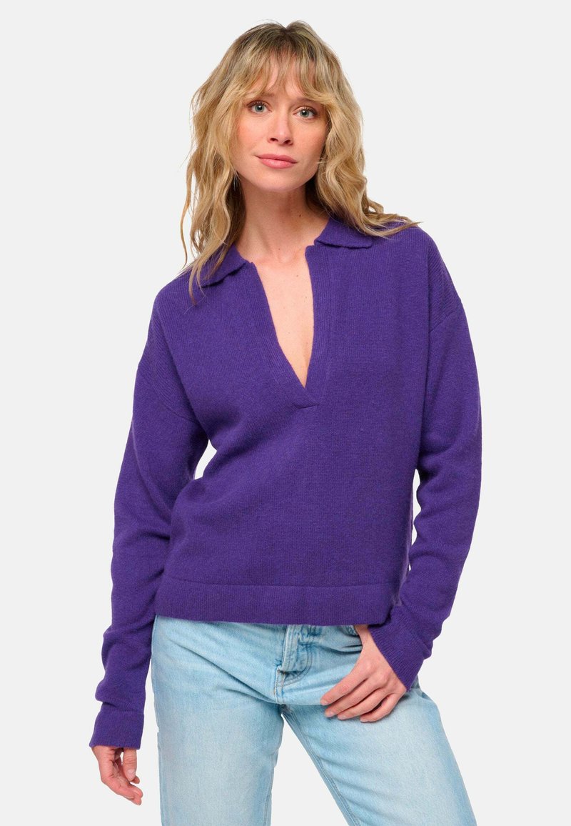 Lila gestrickter Pullover mit Kragen und tiefem V-Ausschnitt. Lange Ärmel und lockere Passform, kombiniert mit hellblauen Jeans.