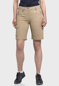 Beige Cargo-Shorts mit schmaler Passform. Mit Seitentaschen, Reißverschlussdetails und umgeschlagenem Saum. Tragen mit dunklen Wanderschuhen.