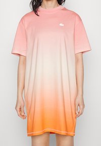 Robe t-shirt surdimensionnée en dégradé de pêche à orange, avec un col rond et un petit logo blanc. Tissu en coton doux, manches courtes.