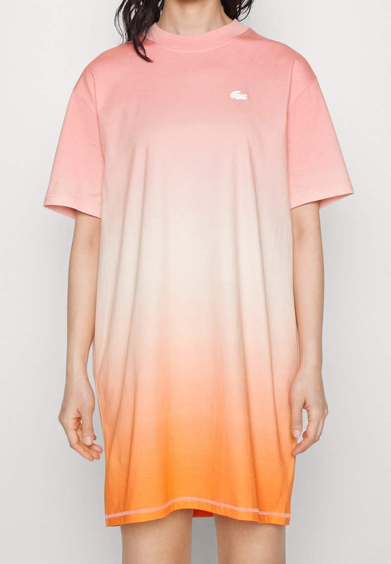 Robe t-shirt surdimensionnée en dégradé de pêche à orange, avec un col rond et un petit logo blanc. Tissu en coton doux, manches courtes.