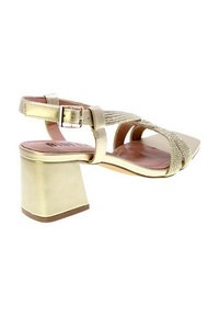 Sandal con tacco largo in oro, con fasce intrecciate e fibbia regolabile alla caviglia. Parte superiore in pelle liscia con una finitura testurizzata.