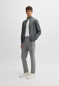 Gray ribbed cardigan, white t-shirt, gray cargo trousers with pockets, and white sneakers. Slim fit design with textured knit.