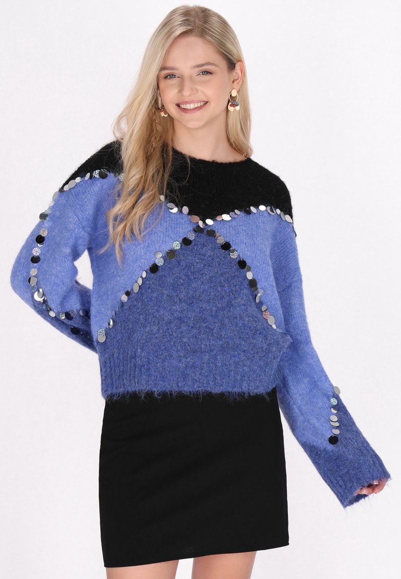 Maglione blu e nero caratterizzato da una texture soffice con paillettes in un motivo geometrico; abbinato a una gonna nera, creando un look stratificato.
