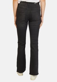 Zwarte uitlopende jeans met een hoge taille, voorzien van twee achterzakken en een gladde textuur. Afgewerkt met subtiele stikdetails.