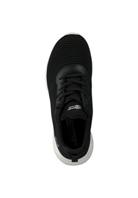 Zapatilla deportiva negra con parte superior de tejido texturizado, cierre de cordones y suela de goma blanca con un diseño de parte trasera redondeada.