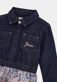 Traper haljina s tamnoplavim gornjim dijelom, kragnom i džepovima; suknja sa svijetlim cvjetnim uzorkom; sadrži logo, kopčanje na dugme i elastičnu struk.