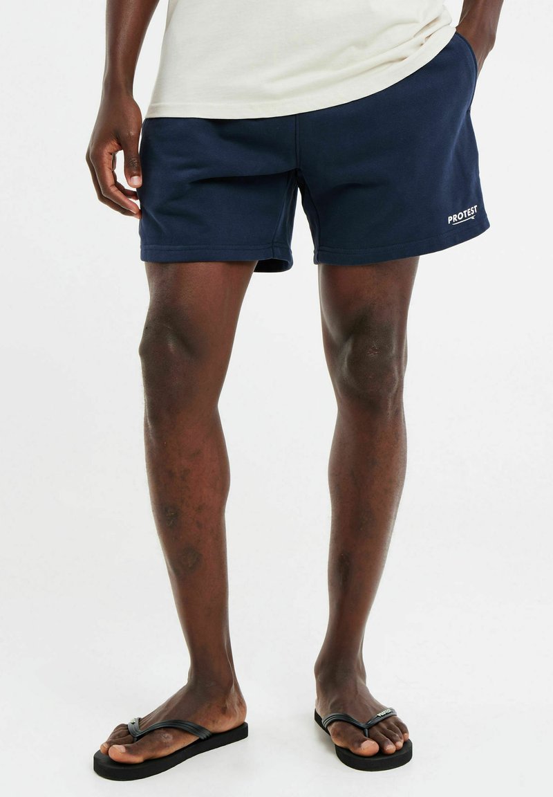 Navyblauwe zwembroek van zacht stof, met een platte tailleband en zijzakken. Logo gedrukt op de zoom. Slippers met dunne bandjes.