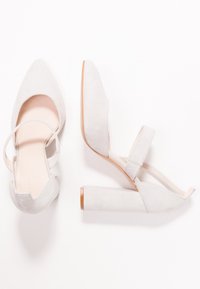 Vita mockaskinn högklackade skor med spetsiga tår, öppen baksida och tunna ankelremmar. Blockklackar med en slät, ljus bas.