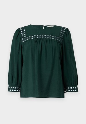 Blusa verde scuro con maniche lunghe a sbuffo, tessuto testurizzato e ritagli decorativi sullo scollo e sui polsini. Chiusura a chiave sulla schiena.