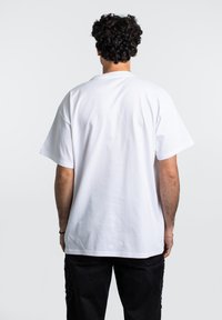 Camiseta de algodón blanca con manga corta y un ajuste relajado, vista desde la parte de atrás. Presenta una textura suave y un diseño sencillo.