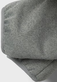 Couverture grise texturée avec un design tissé et une bordure lisse. Le tissu a une apparence douce et confortable, adapté pour la literie ou la décoration.