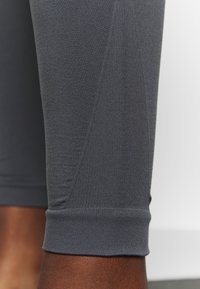 Grå sportleggings tillverkade av elastisk, mjuk tyg, med en figurnära form och en avskuren fåll vid ankeln.