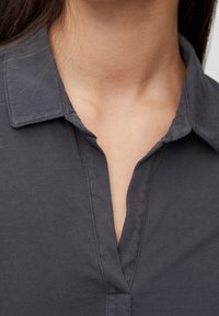 Närbild av en persons nacke och övre bröst med en mörkgrå skjorta med krage och öppen V-hals.