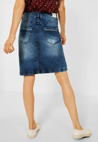 Denimkjol i mörkblått med en figursydd silhuett, rak skärning, två bakfickor och en fåll som sitter strax ovanför knät.