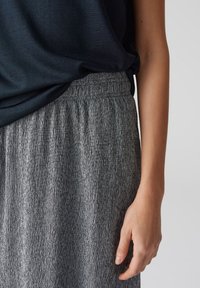 Grauer, strukturierter Rock mit einem elastischen Bund, kombiniert mit einem dunklen Oberteil. Der Rock hat vertikale Linien, die ein dezentes Muster bilden.