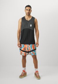Top atlético sin mangas en negro y gris con un logo y pantalones cortos de patrón multicolor que presentan diseños ondulados en naranja y azul.