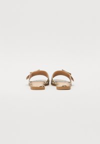 Platte sandaal met een beige band, met een patroon op de voetbed en een lichtbruine zool. Beschikt over een verstelbare gespsluiting en geweven details.