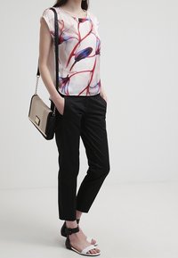 Halenka s květinovým vzorem v bílé barvě, s červenými a modrými pruhy, spárovaná s černými slim-fit kalhotami. Doplněk zahrnuje černou a béžovou kabelku.