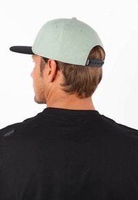 Casquette vert clair avec une visière noire, dotée d'une fermeture snapback et d'un logo discret sur le côté. Tissu texturé, forme structurée.