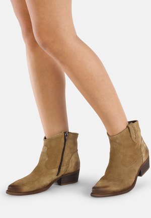 Stivaletti alla caviglia in suede color sabbia con tacco basso in legno, dotati di una cerniera laterale, punta appuntita e cuciture decorative lungo la parte superiore.
