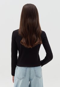 Schwarzes langärmliges Oberteil mit tailliertem Design, gerippter Textur und rundem Halsausschnitt, kombiniert mit hellblauen High-Waist-Jeans.