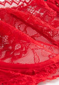 Tissu en dentelle rouge avec motifs floraux et texture en maille transparente, montrant des coutures détaillées et des plis doux.
