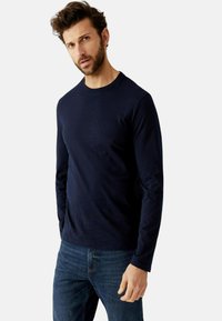 Dunkelblaues Langarm-T-Shirt aus Baumwolle, mit rundem Halsausschnitt und taillierter Passform, kombiniert mit blauen Jeans.