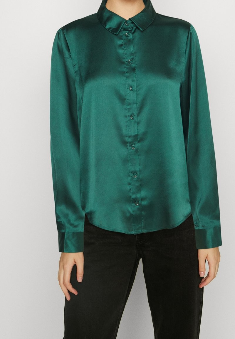 Chemise en satin vert avec un col classique, manches longues et fermeture à boutons à l'avant. Présente une texture lisse et un ourlet arrondi.