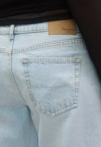 Ανοιχτό μπλε τζιν τζιν με πίσω τσέπη και καφέ δερμάτινο ταμπελάκι με την επιγραφή "Pepe Jeans London." Διακρίνονται ραφές στη υφασμάτινη επιφάνεια.