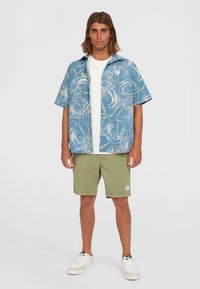 Blauw gestreept shirt met korte mouwen en witte ontwerpen, gecombineerd met olijfgroene shorts en witte sneakers. Casual zomerset.
