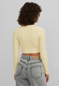 Haut court jaune à manches longues côtelées, associé à un jean en denim gris clair taille haute. Le haut présente un col rond et une coupe ajustée.