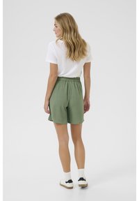Gröna shorts i strukturerad textil, elastisk midja, midjehöjd, i kombination med en vit T-shirt och vita sneakers med svarta detaljer.