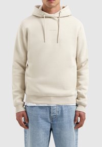 Beige pullover hoodie gemaakt van zachte stof. Voorzien van een voorzak met kangoeroe-style, een capuchon met trekkoord en ribgebreide manchetten en onderzoom. Minimale branding.