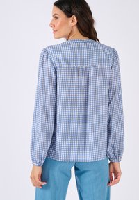 Blusa a quadretti azzurri e bianchi, maniche lunghe a sbuffo, polsini elasticizzati, dettaglio arricciato sulla schiena, realizzata in tessuto leggero.