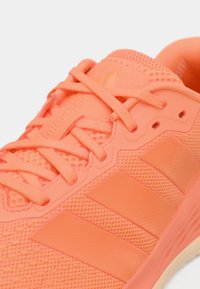 Λαμπερό κορράλι αθλητικό παπούτσι με δίχτυ πάνω μέρος, καουτσούκ σόλα και εμφανές σχέδιο με τρεις ρίγες. Διαθέτει επίπεδα κορδόνια και υφή λεπτομέρειες.