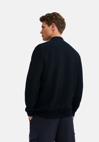 Black textured jacket with a ribbed collar and cuffs, featuring a fitted design and pockets, worn with dark patterned pants.