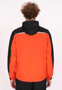 Orange og sort jakke med hætte, der har refleksdetaljer og elastiske manchetter. Fremstillet af letvægts, vandafvisende materiale.