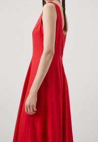 Robe rouge sans manches avec un design fluide, présentant une texture lisse et un corsage ajusté se transformant en une jupe évasée.