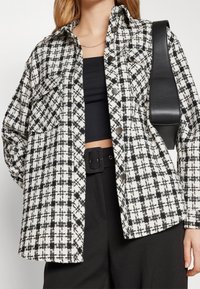 Lettet ternet jakke i sort og hvidt stof, med knaplukning foran, to brystlommer og en afslappet pasform.