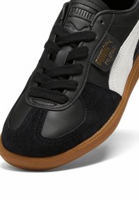 Gros plan de la basket Puma Palermo noir et blanc avec des lacets noirs, des empiècements en daim et en cuir, et une semelle en gomme naturelle.