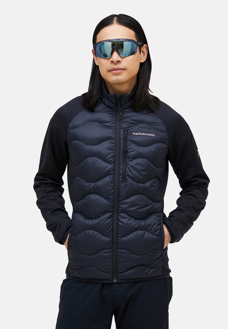 Schwarze isolierte Jacke mit gestepptem Muster auf der Vorderseite, kombiniert mit Ärmeln aus schwarzem Stretchstoff. Verfügt über eine mit Reißverschluss verschließbare Brusttasche.