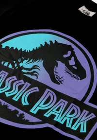 Jurassic Park logo with a silhouetted T-Rex head inside a purple and blue circular border on a black fabric background.