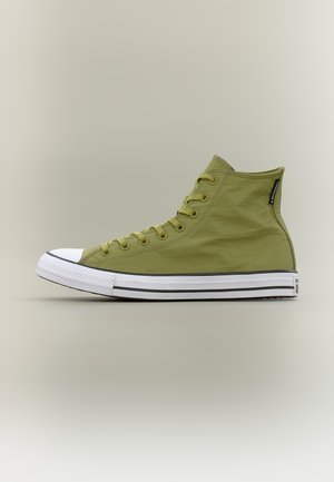 Baskets montantes vert olive avec embout et semelle en caoutchouc blanc, détails à rayures noires et une étiquette en tissu près du col de la cheville.