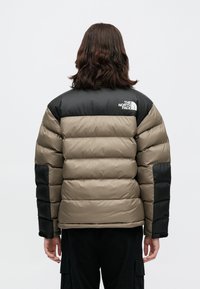 Kurtka puchowa w kolorystyce beżowo-czarnej, pikowana, z logo The North Face na górnej części pleców i rękawach.