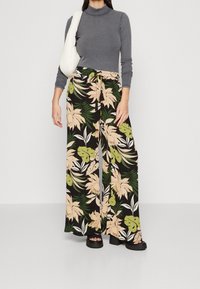 Pantalon à jambes larges noir avec un motif floral en rose, vert et crème. Associé à un haut gris à manches longues côtelé et à un sac blanc.