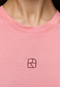 Rosa kortärmad t-shirt i mjukt tyg, med rund halsringning och en liten svart broderad logotyp på bröstet.