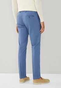 Lichtblauwe broek van gladde stof, met achterzakken en een getailleerde pasvorm. Gecombineerd met beige instap-schoenen.